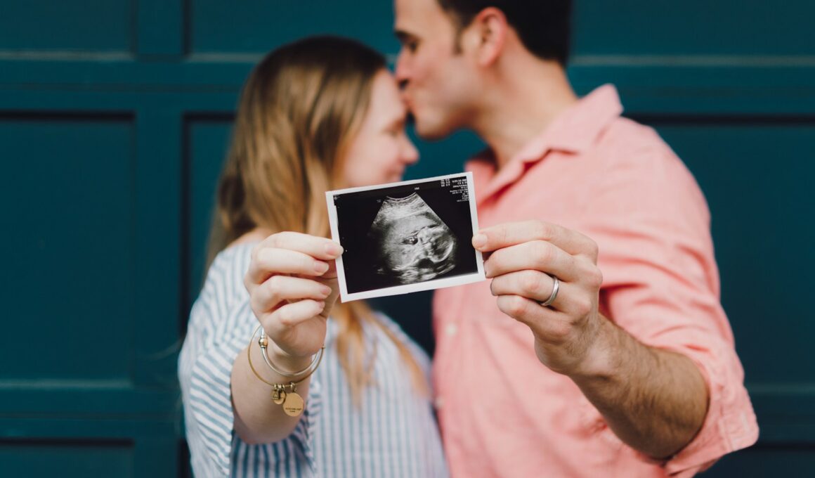 man kissing woman's forehead white holding ultrasound photo